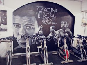 Row of cycling machines in 'Fight Gym' with a fighter mural in the background.